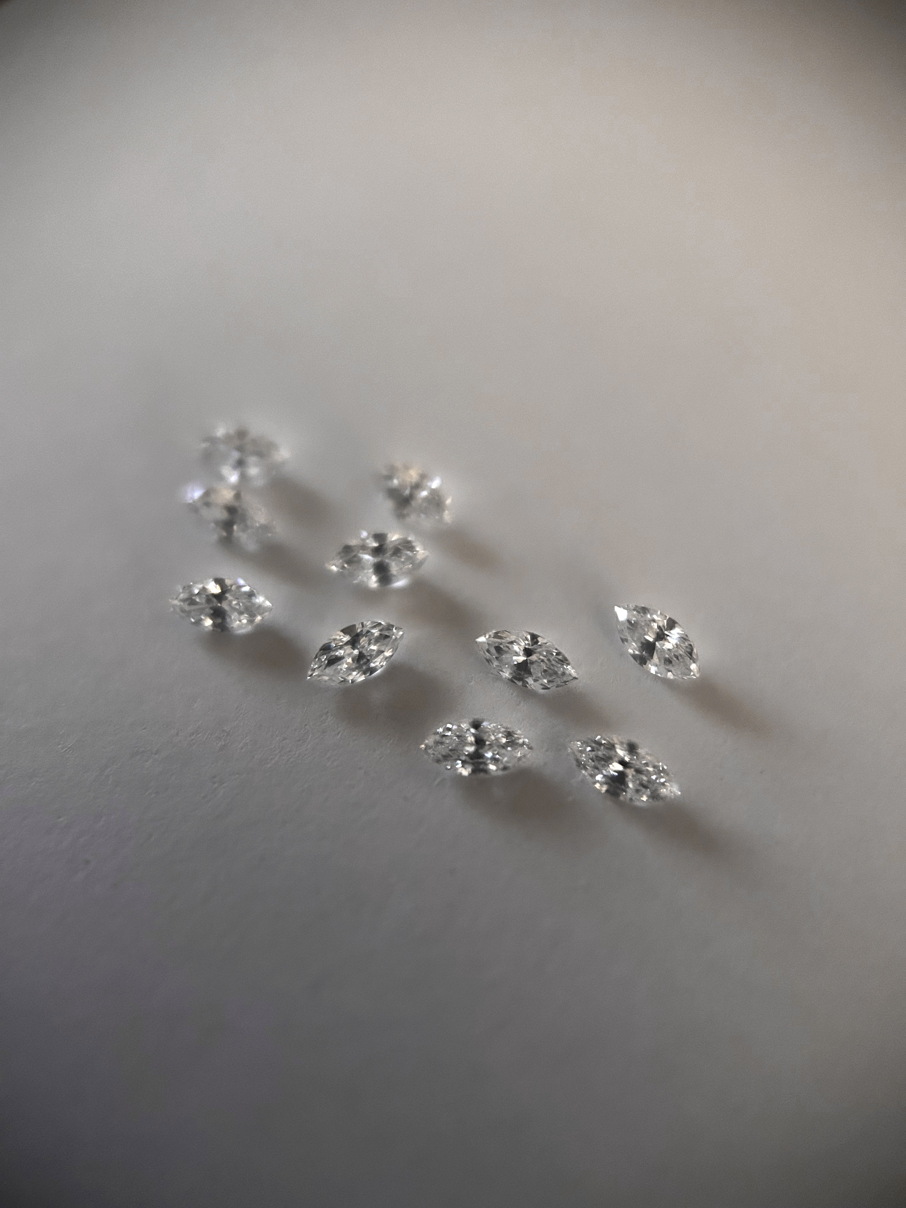 Diamants taille navette et diamants ronds disposés sur une surface claire pour la création d’une bague de fiançailles.